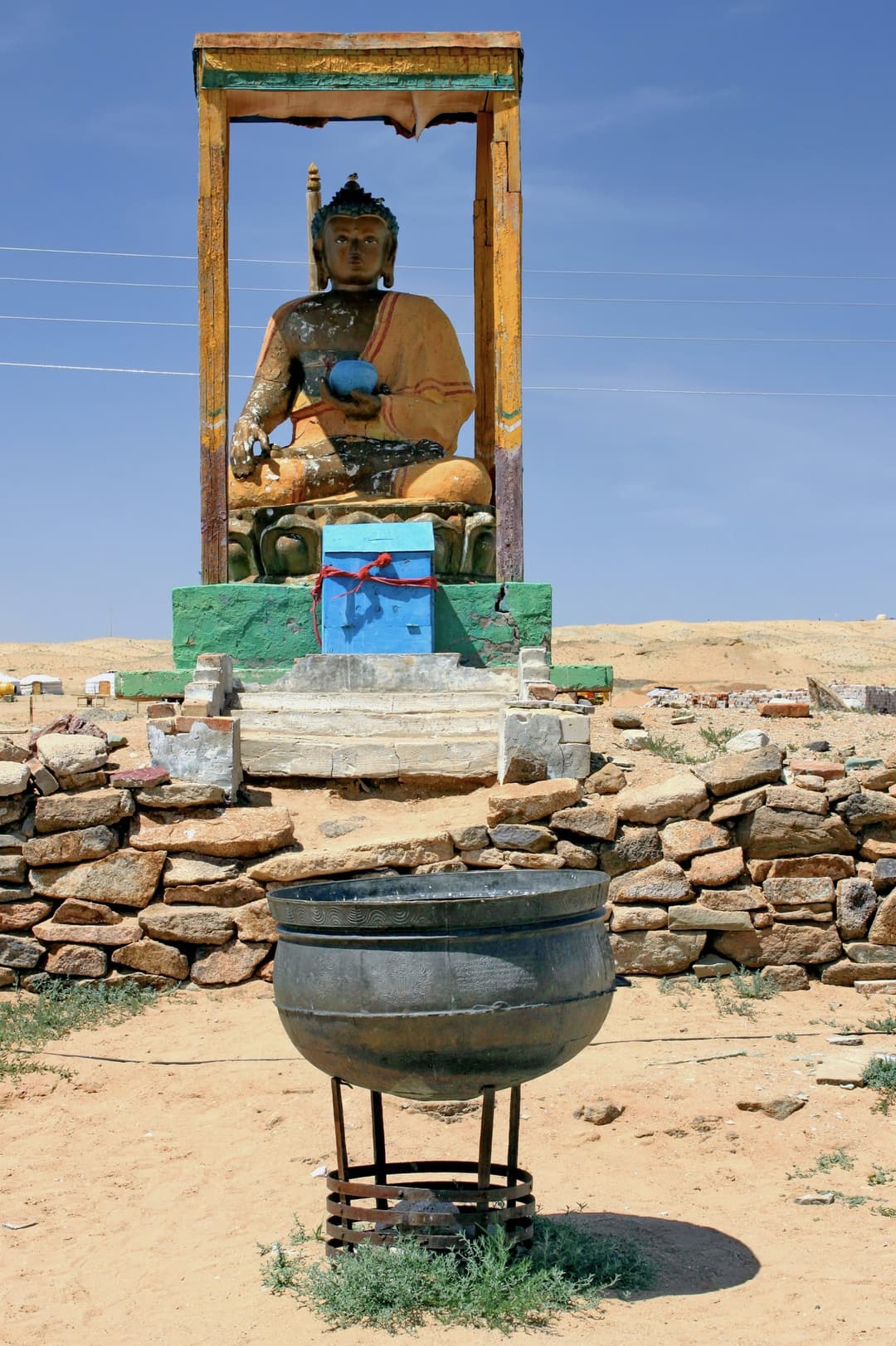 Front view of a seated Buddha shrine and large metal cauldron in daylight.