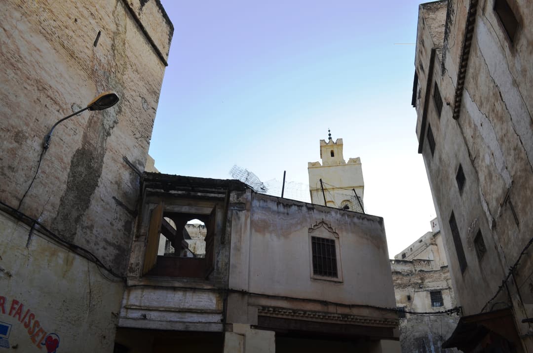 Low-angle view of the minaret rising above medina alley buildings