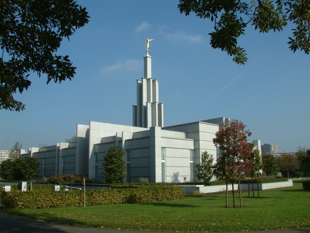 Exterior view of The Hague Netherlands Temple framed by tree branches.