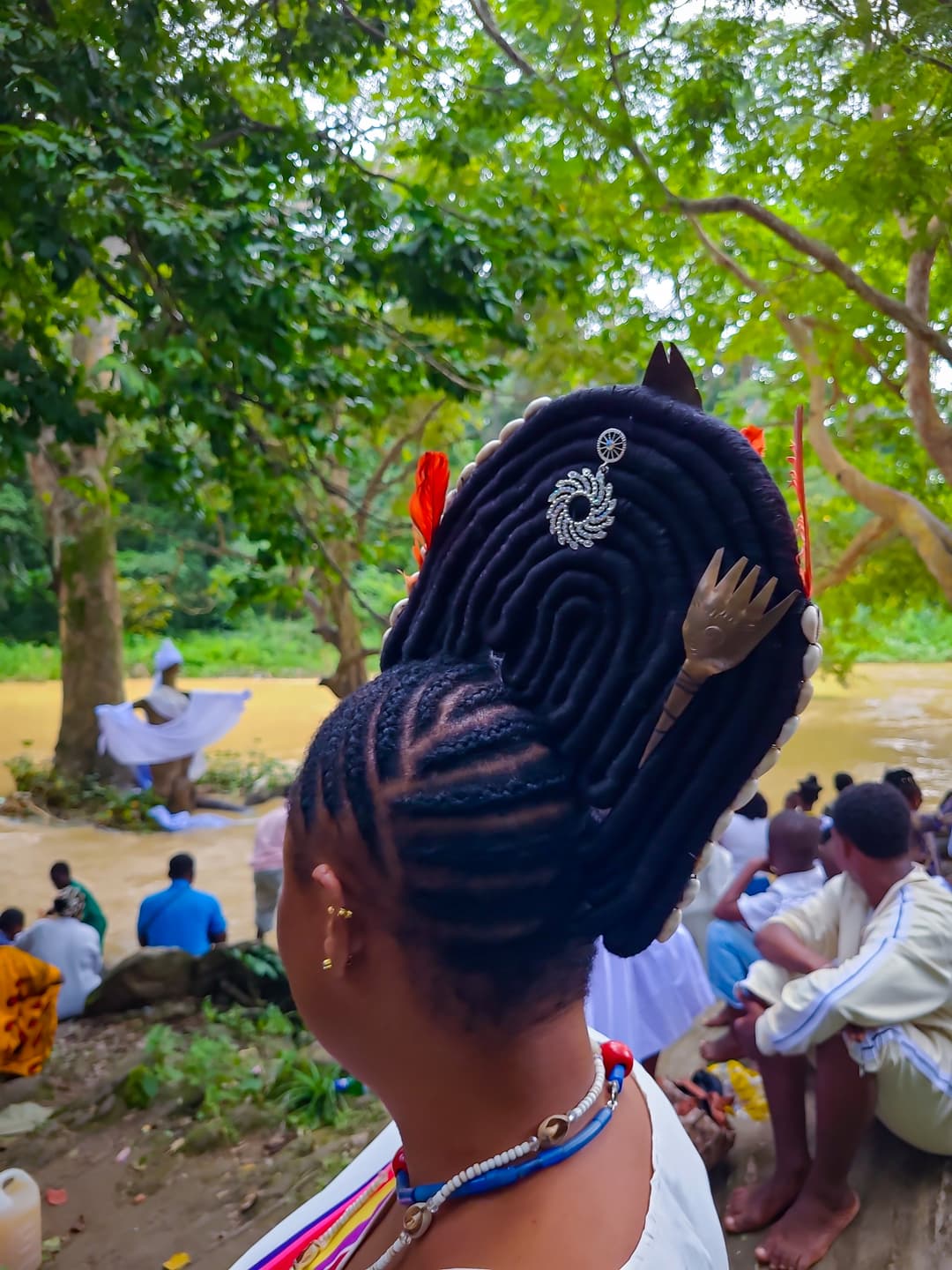 Devotee with ornate traditional hairstyle overlooking the Osun River