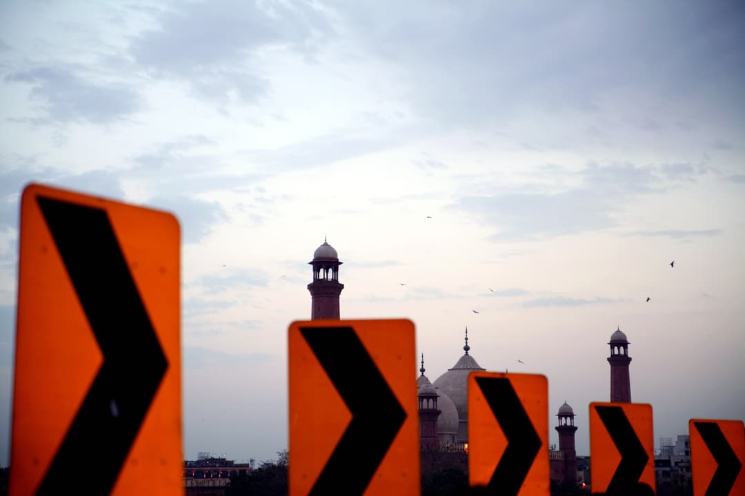 Badshahi Mosque domes and minarets viewed behind roadside signs at dusk.