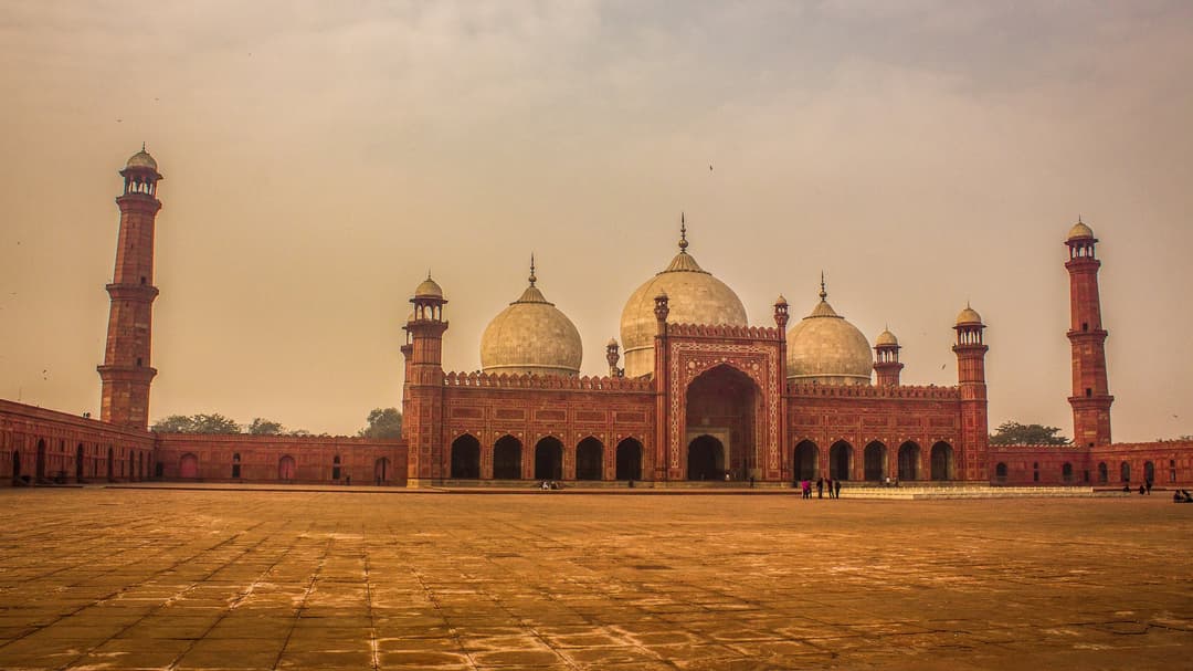 Wide view across the vast courtyard to the prayer hall and marble domes.