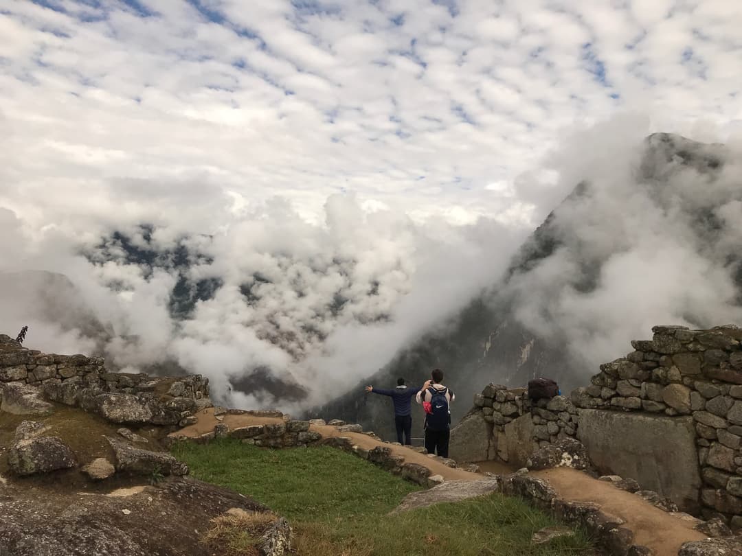 Visitors overlooking misty mountains from stone ruins at Machu Picchu.