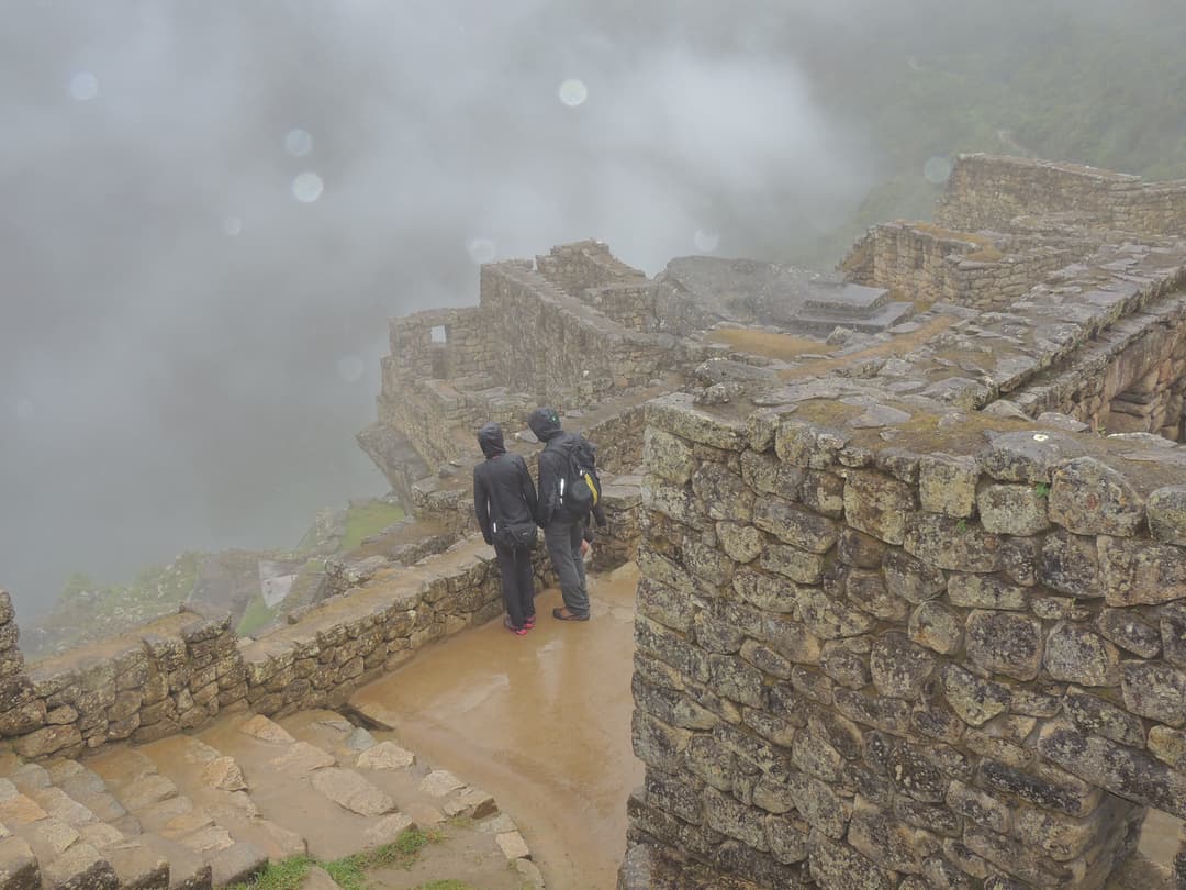 Visitors overlooking mist-shrouded stone ruins at Machu Picchu.