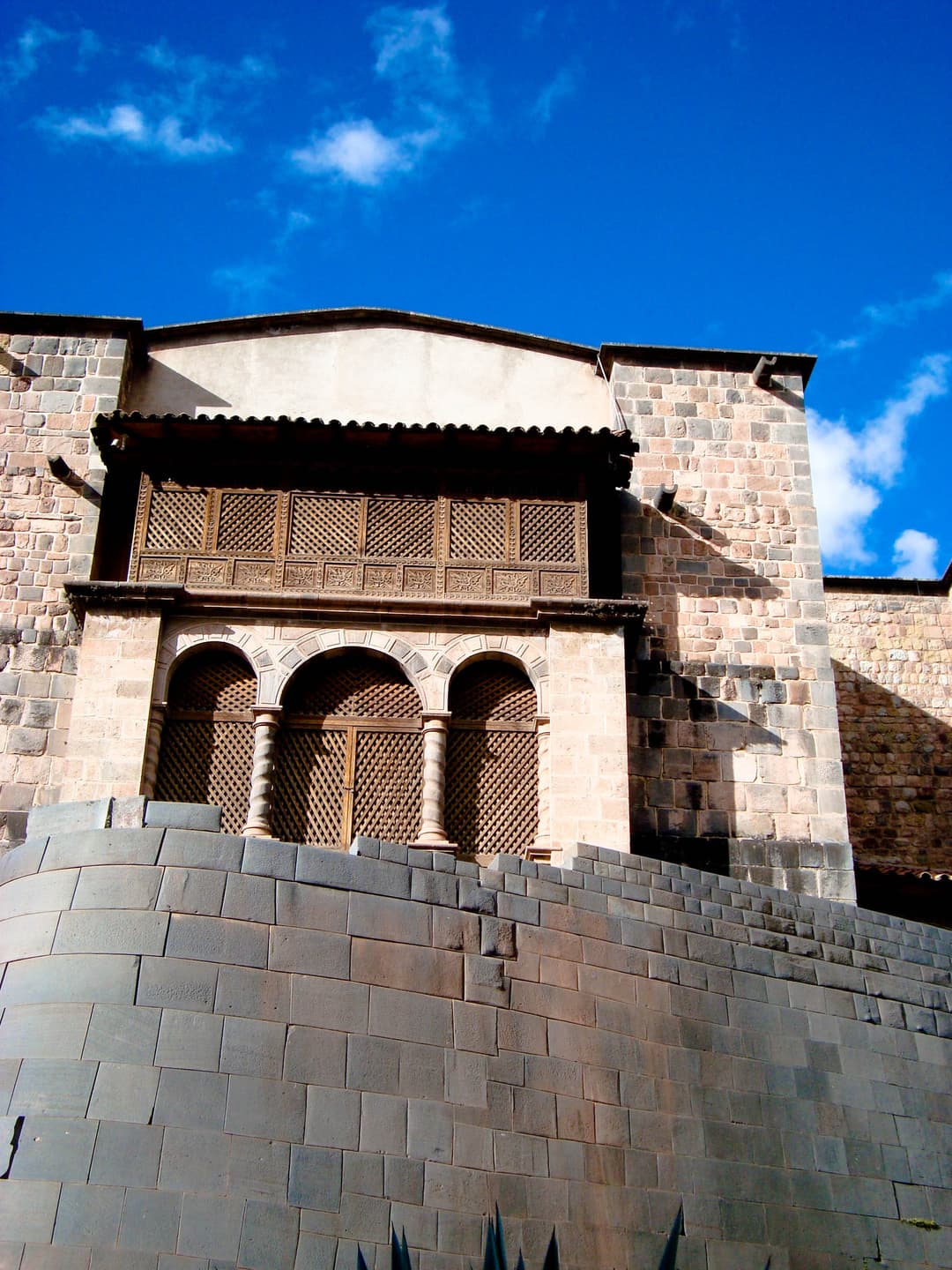 Low-angle view of the curved Inca wall beneath a colonial balcony.