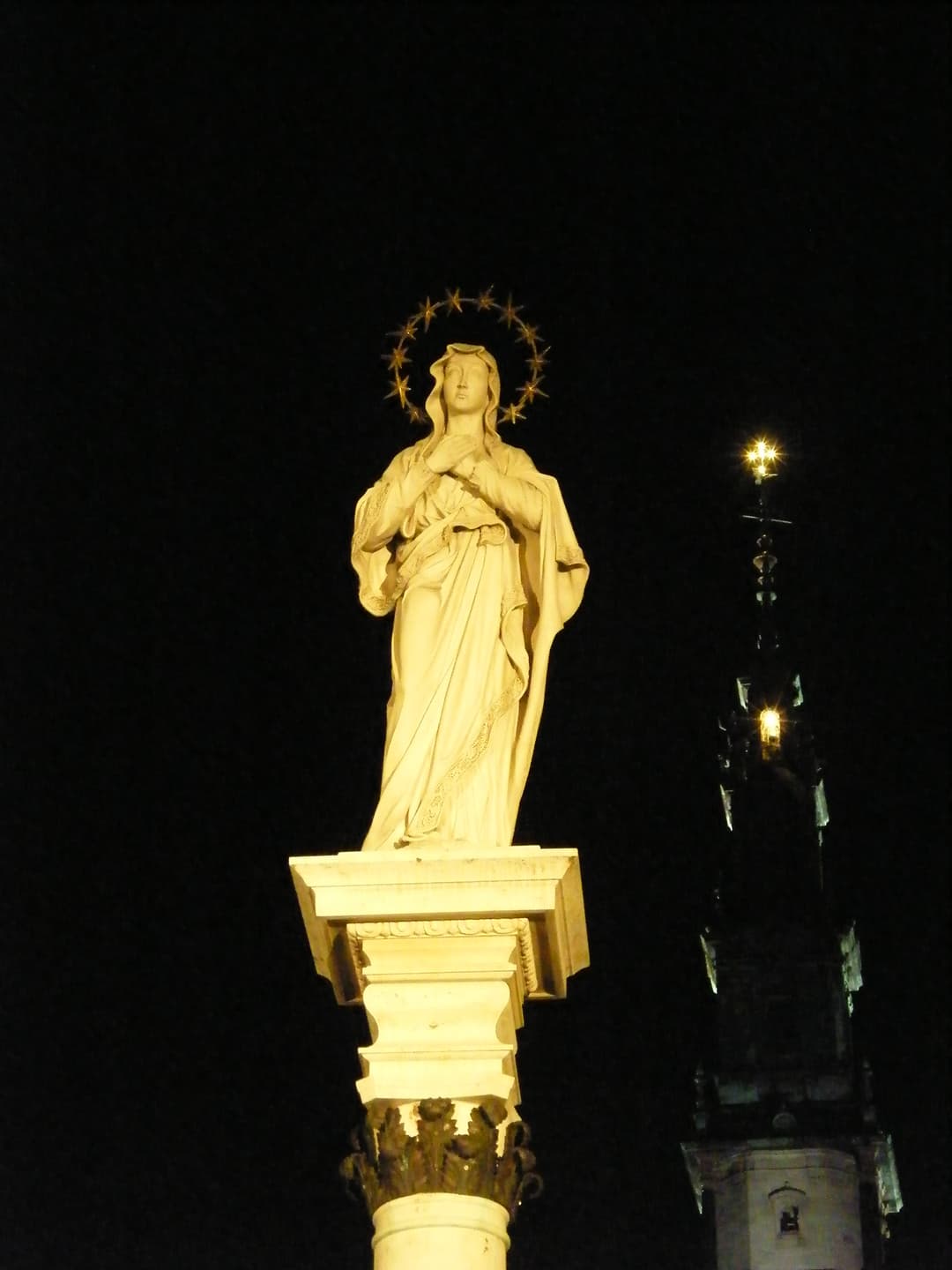 Statue of the Virgin Mary on a column at night with the Jasna Góra tower