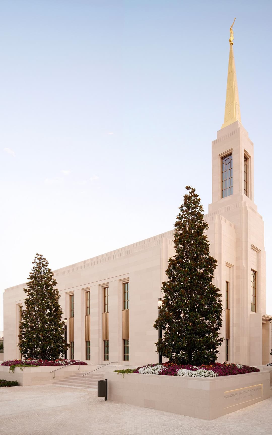 Angled exterior of Lisbon Portugal Temple, golden spire, magnolia trees, flower beds.