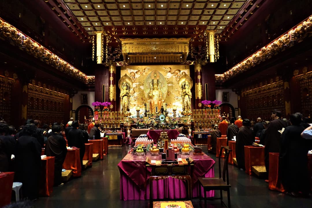 Main shrine hall interior with golden Buddha statues and worshippers at prayer.