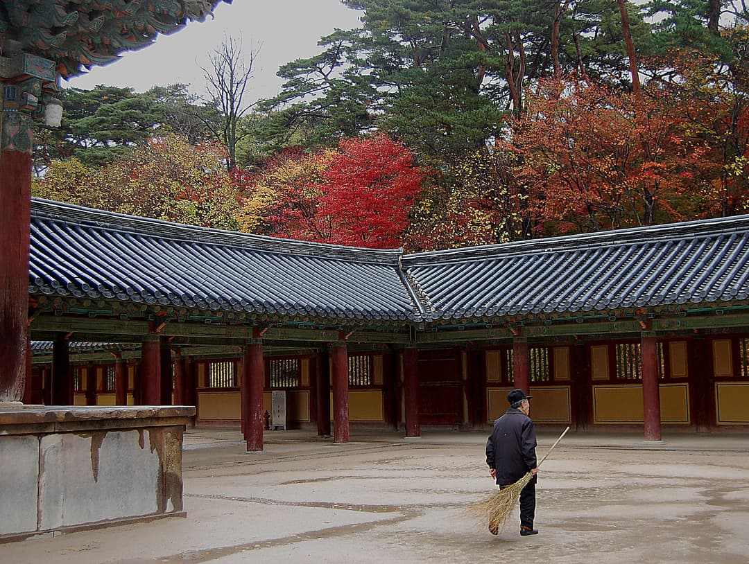 A worker sweeps the Bulguksa Temple courtyard framed by autumn foliage.