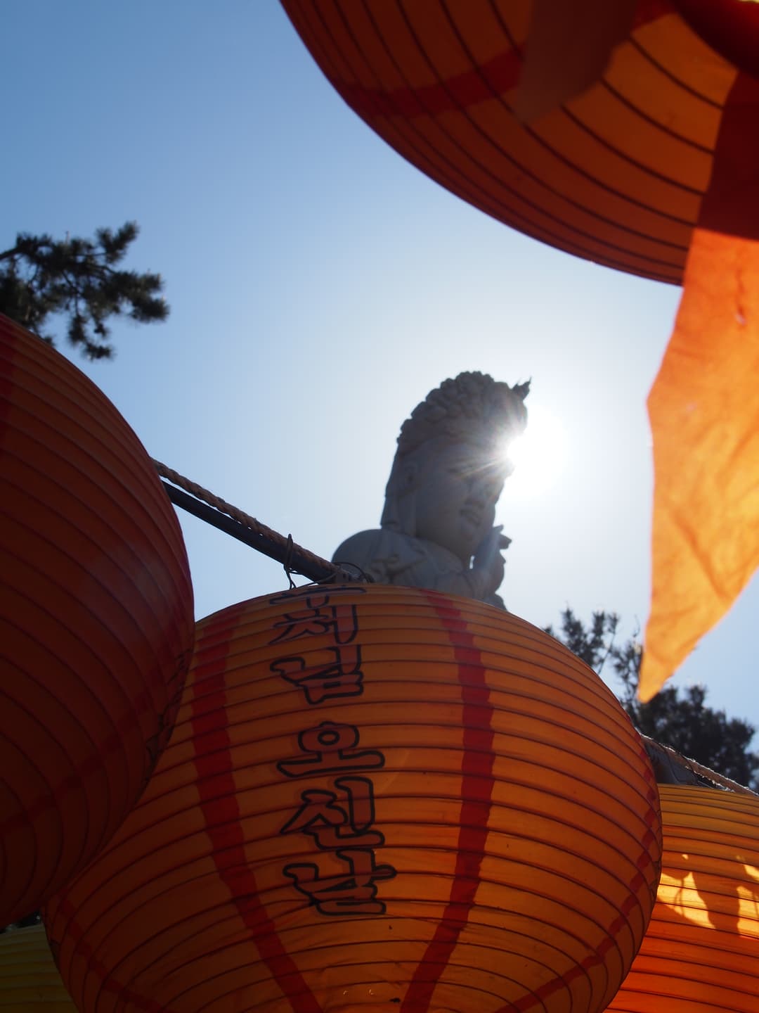 Low-angle view of paper lanterns framing the backlit stone Gwaneum statue.