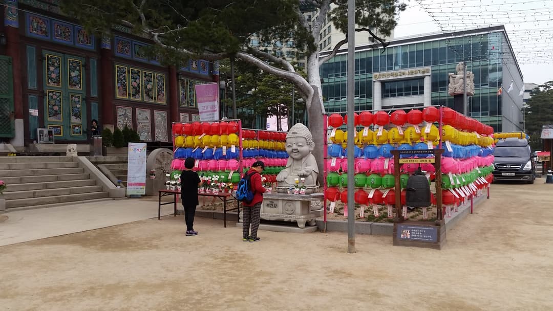 Stone Buddha surrounded by colorful lanterns in the Jogyesa Temple courtyard.