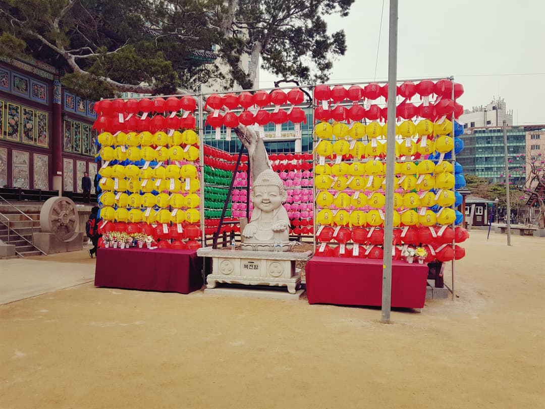Stone Buddha statue amid colorful lanterns in the Jogyesa Temple grounds.