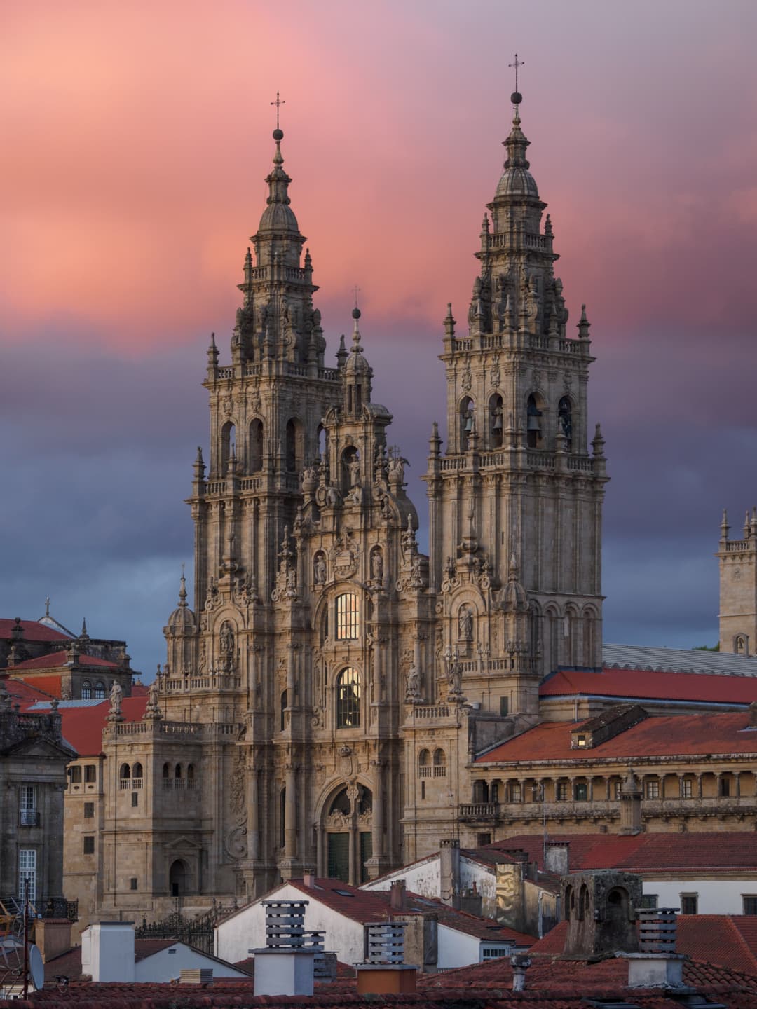 Obradoiro facade and twin towers above city rooftops at sunset