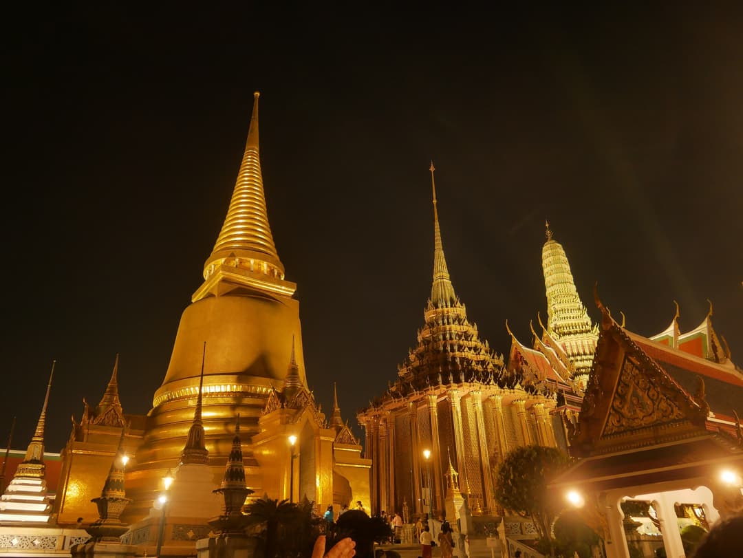 The golden stupa and spires of Wat Phra Kaew illuminated at night.