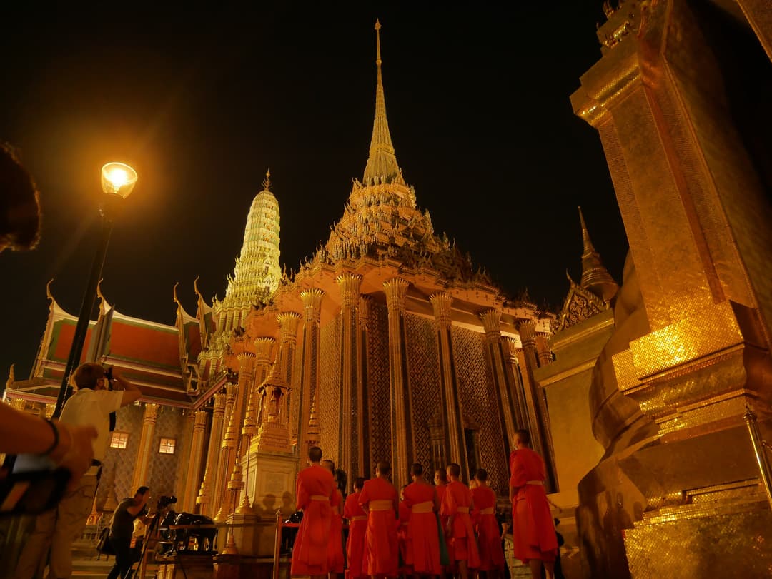 Monks gathered before the illuminated golden spires of Wat Phra Kaew at night.