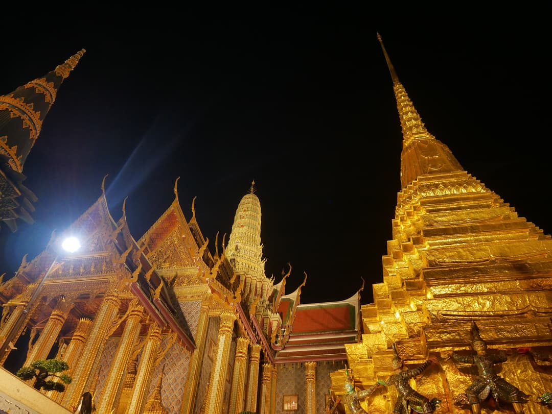 Low-angle view of the illuminated golden chedi at Wat Phra Kaew at night.