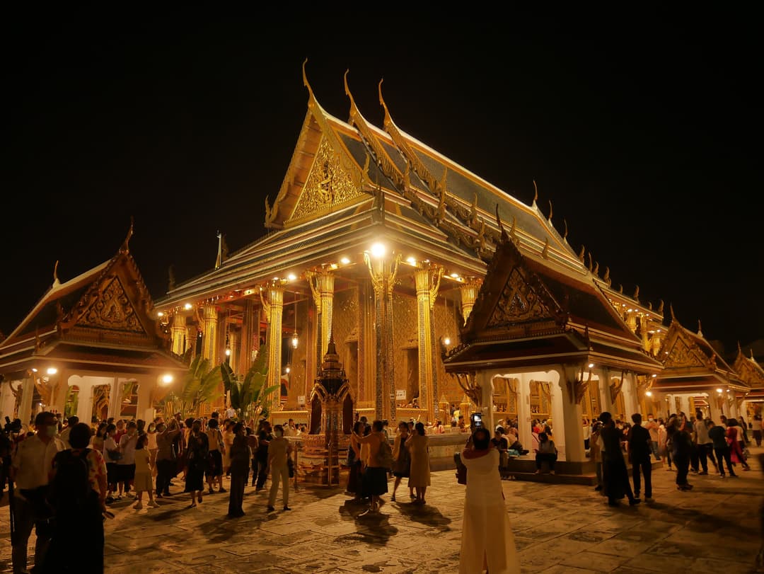 Night view of the illuminated Phra Ubosot at Wat Phra Kaew with visitors.