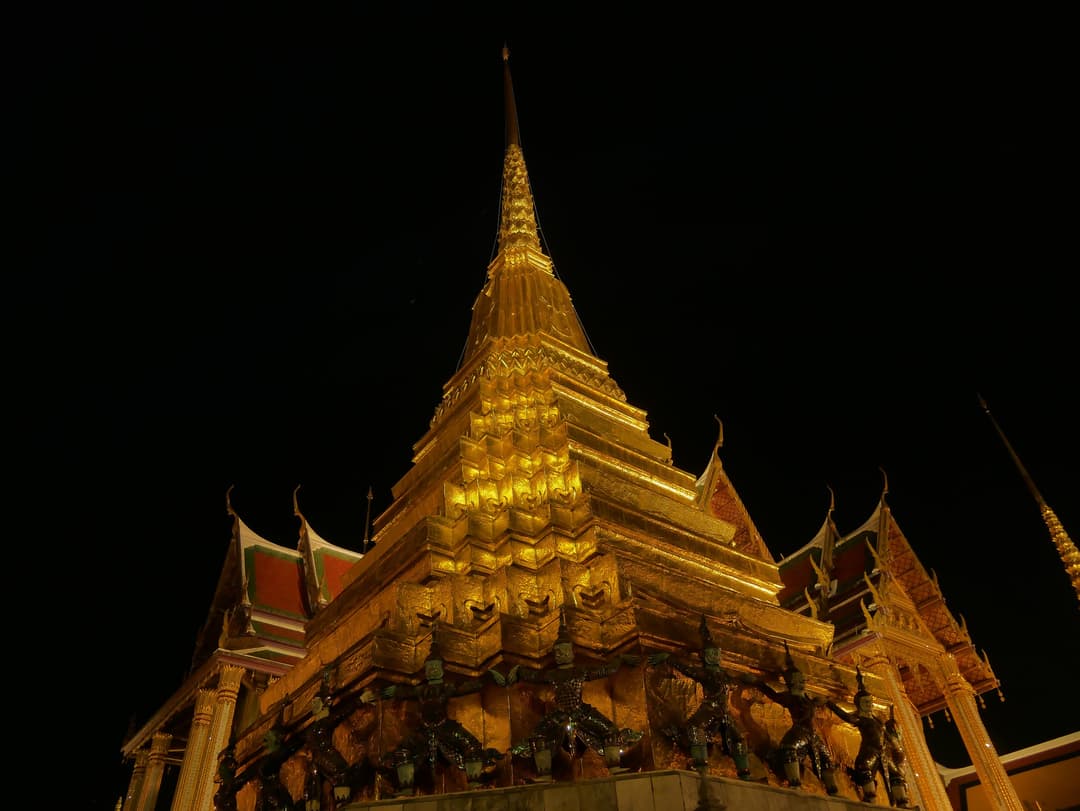 Low-angle view of the illuminated golden chedi at Wat Phra Kaew at night.