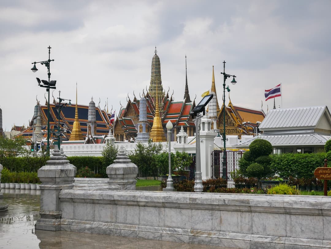 Spires and prangs of Wat Phra Kaew viewed beyond a marble wall.