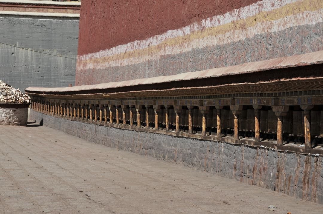 Row of prayer wheels along the striped fortress wall at Sakya Monastery.