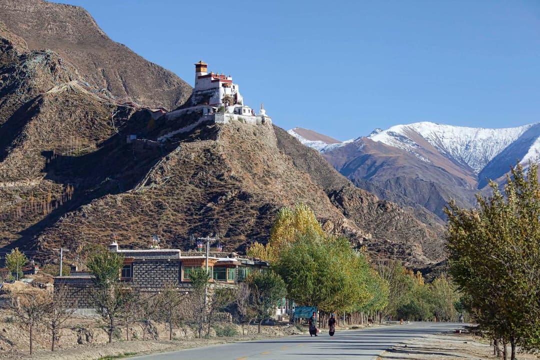 Wide view of Yumbulagang perched on a ridge with snow-capped peaks behind.