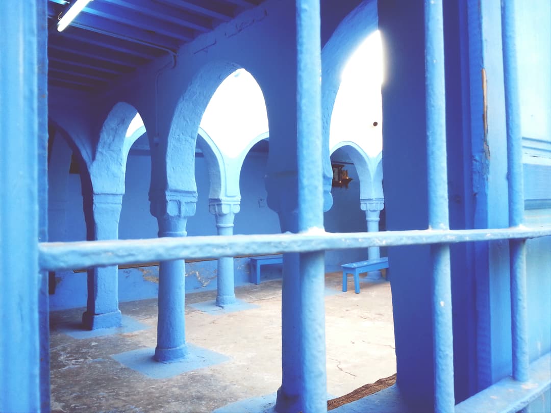 Blue-painted arches and colonnade viewed through a window grille