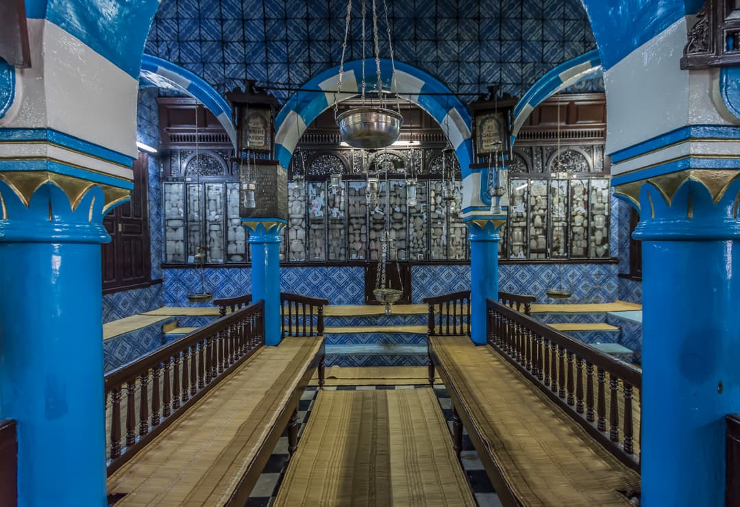 Prayer hall interior with blue arches, wooden benches, and hanging lamps