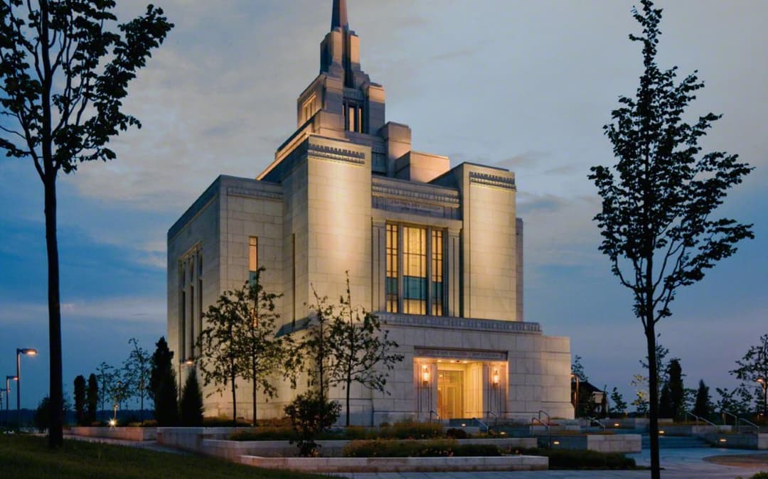 Exterior view of the illuminated Kyiv Ukraine Temple and spire at twilight.