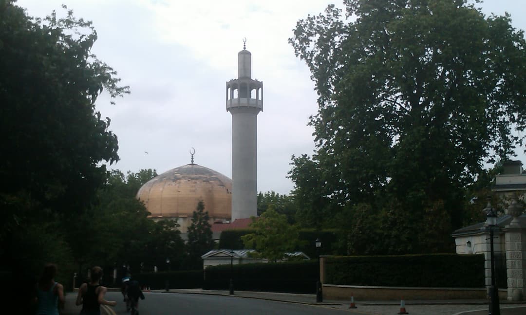 Exterior street-level view of the gilded dome and minaret framed by trees.