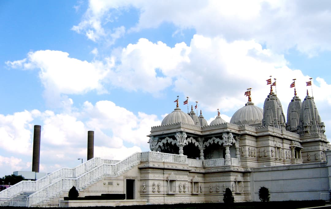 Side view of Neasden Temple showing white stone domes, spires, and grand stairs.