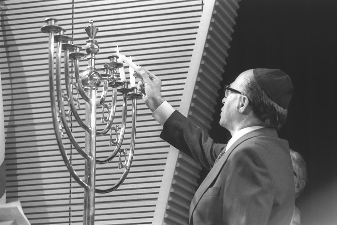 A man lighting a silver Hanukkah menorah inside Western Marble Arch Synagogue.