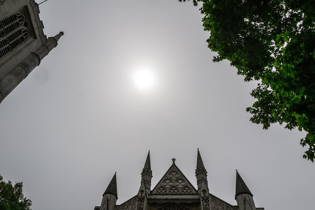 Low-angle view of Westminster Abbey spires framing the sun in a hazy sky.