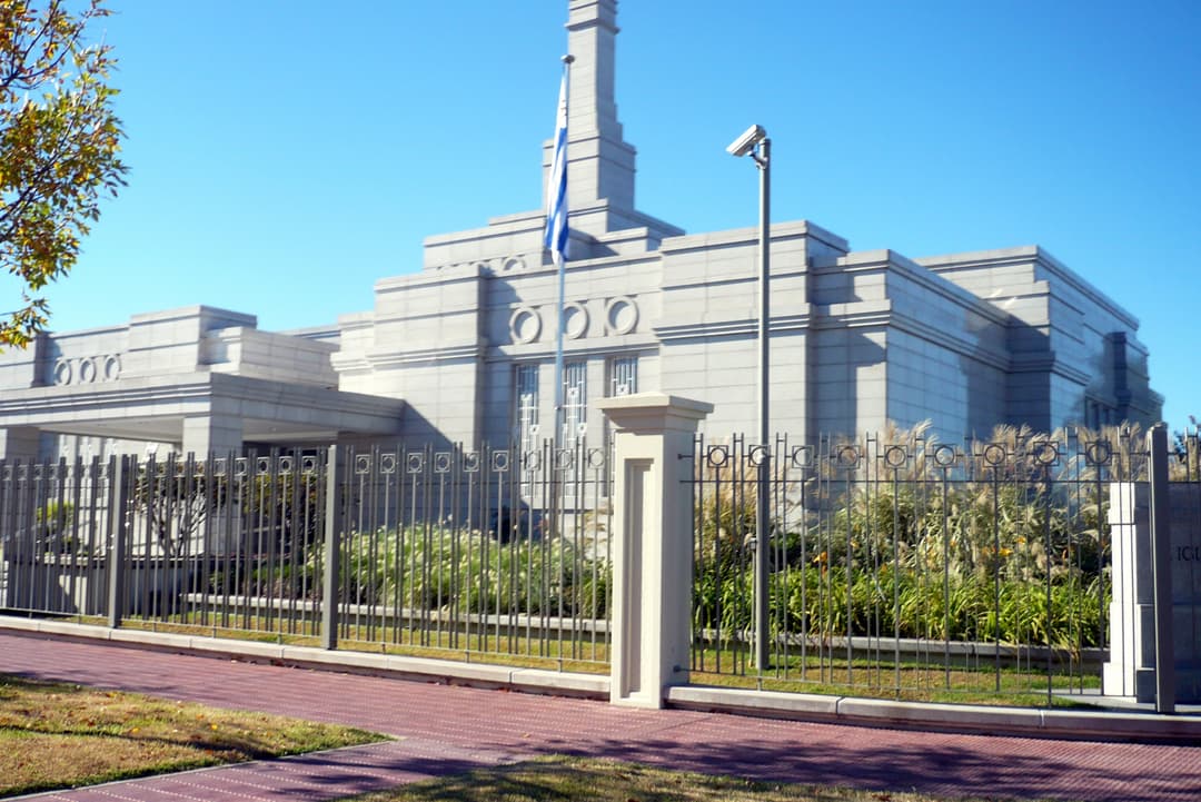 Montevideo Uruguay Temple exterior with spire, flag, and grounds on a sunny day.