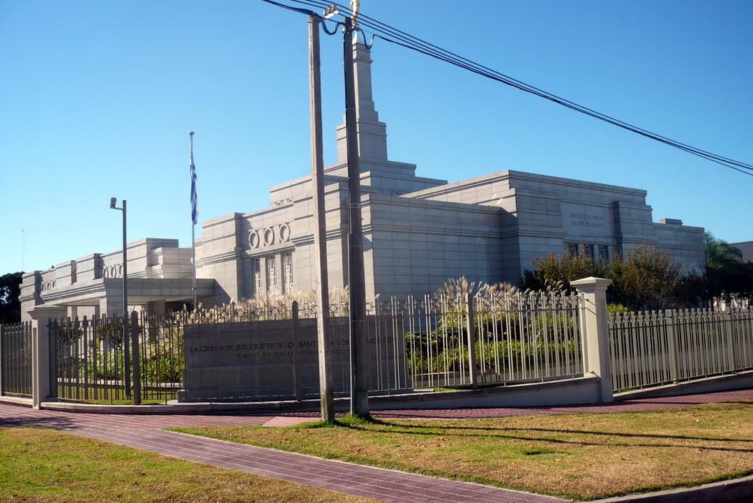 Front-left exterior of Montevideo Uruguay Temple with spire and flag, clear day.