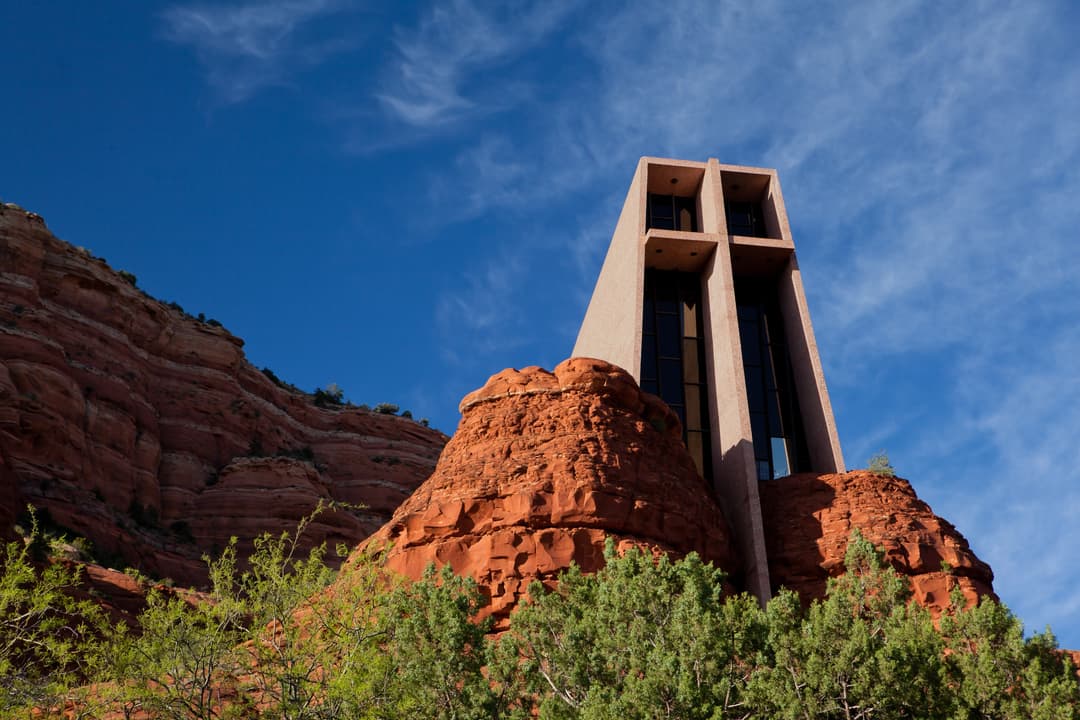 Low-angle exterior view of the Chapel of the Holy Cross built into red rock.