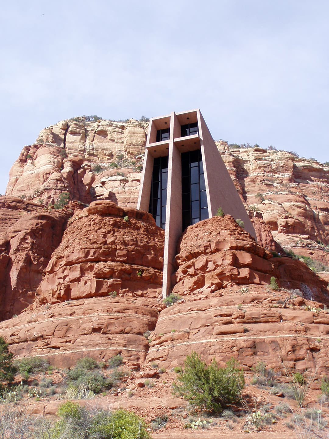 Low-angle view of the Chapel of the Holy Cross rising from red rock cliffs.