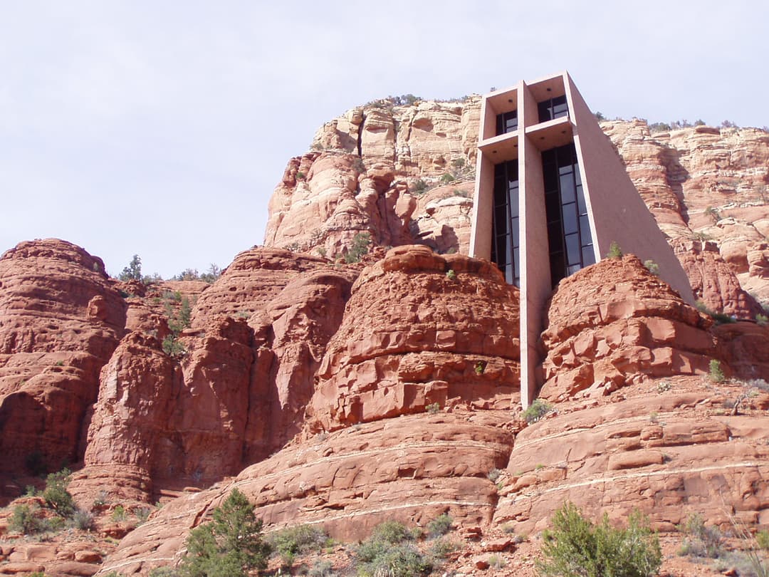 Low-angle view of the Chapel of the Holy Cross built into red rock cliffs.