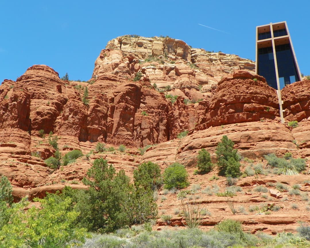 Low-angle view of the Chapel of the Holy Cross built into red sandstone rocks.