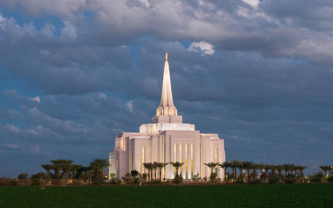 Illuminated Gilbert Arizona Temple spire at twilight, with a cloudy sky and field.