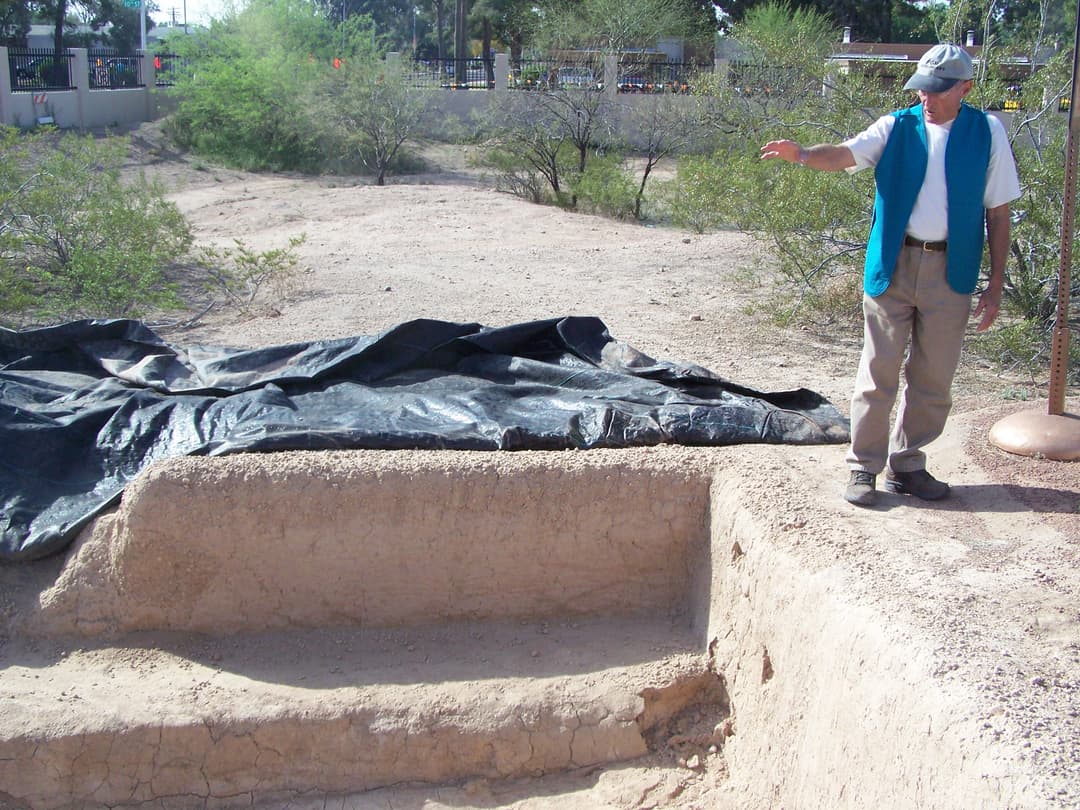 Archaeological excavation pit and earthwork with a presenter pointing.
