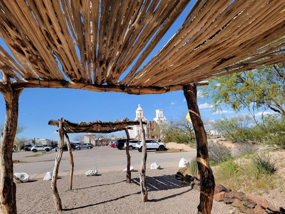Mission San Xavier del Bac framed by a traditional wooden ramada.