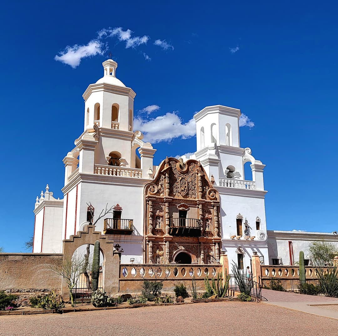 Front facade of Mission San Xavier del Bac under a bright blue sky.