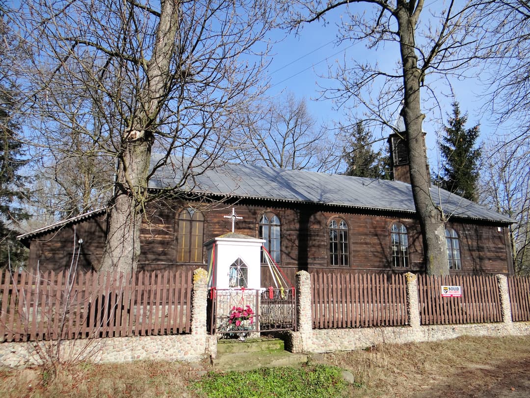 Exterior view of the wooden chapel and roadside shrine behind a fence