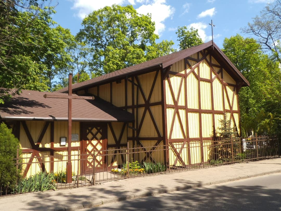Exterior view of the yellow timber-framed chapel and cross on a sunny day.
