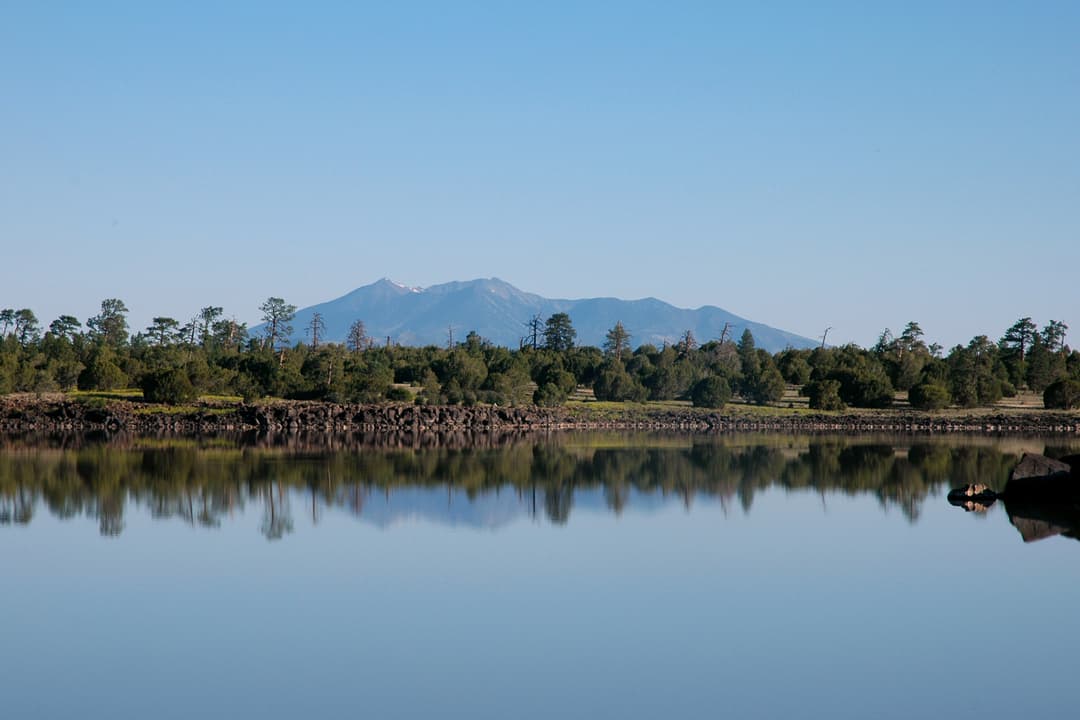 Distant San Francisco Peaks reflected across calm lake waters.