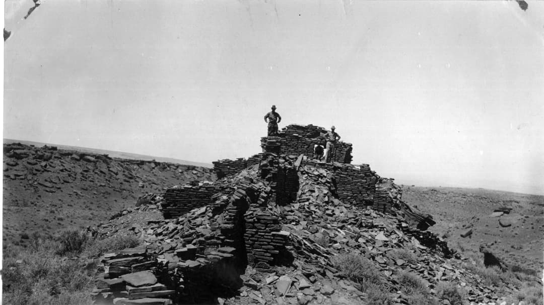 Historic wide-angle view of Wupatki Pueblo stone ruins with figures.