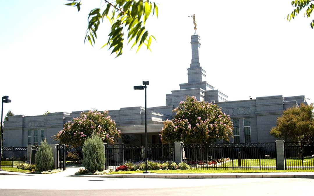 Daytime exterior of Fresno California Temple with spire, Angel Moroni, and flowering trees.