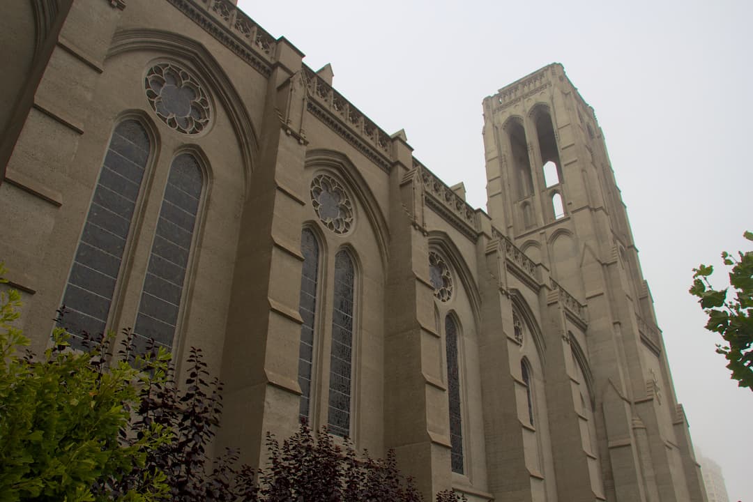 Low-angle view of Grace Cathedral's side facade and tower on a foggy day.