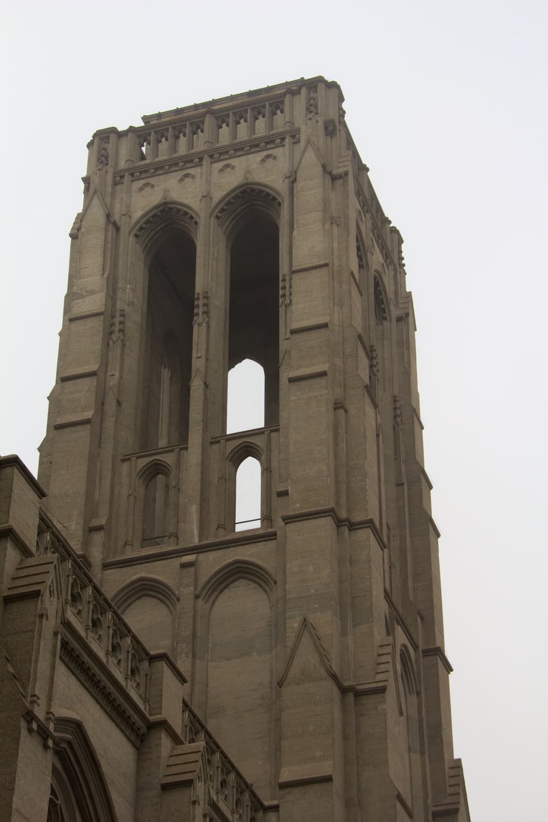 Low-angle view of the Gothic Revival bell tower against an overcast sky.