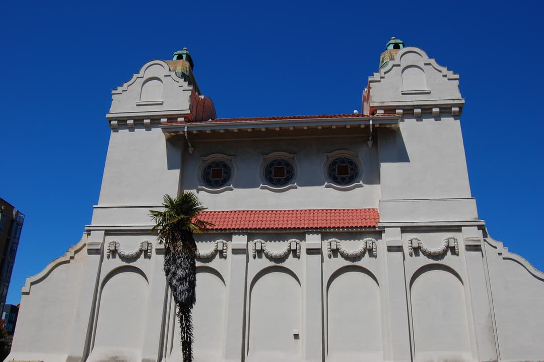 Low-angle view of the Mission Revival facade, twin towers, and a palm tree